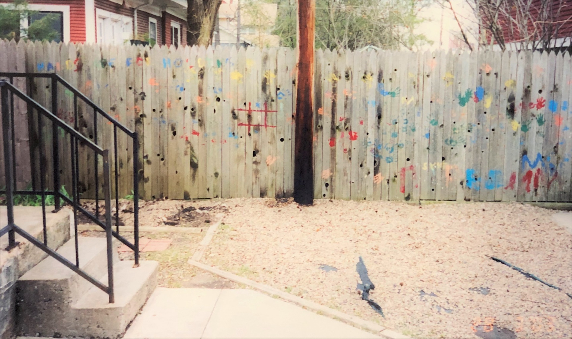 Brightly colored children’s handprints painted along a weathered wooden fence.