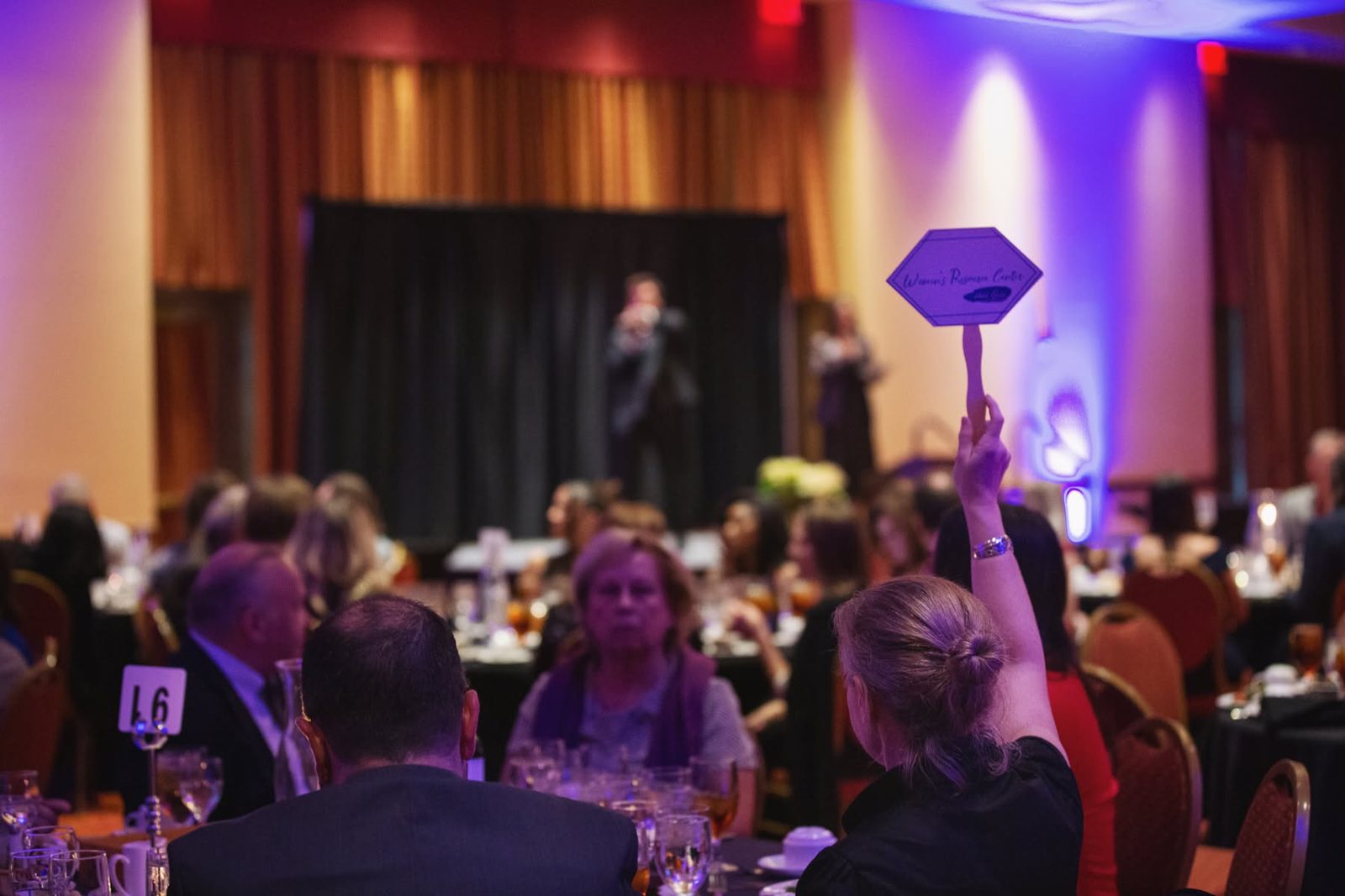 Guests at a Women&rsquo;s Resource Center fundraising gala, one raising a bid paddle.